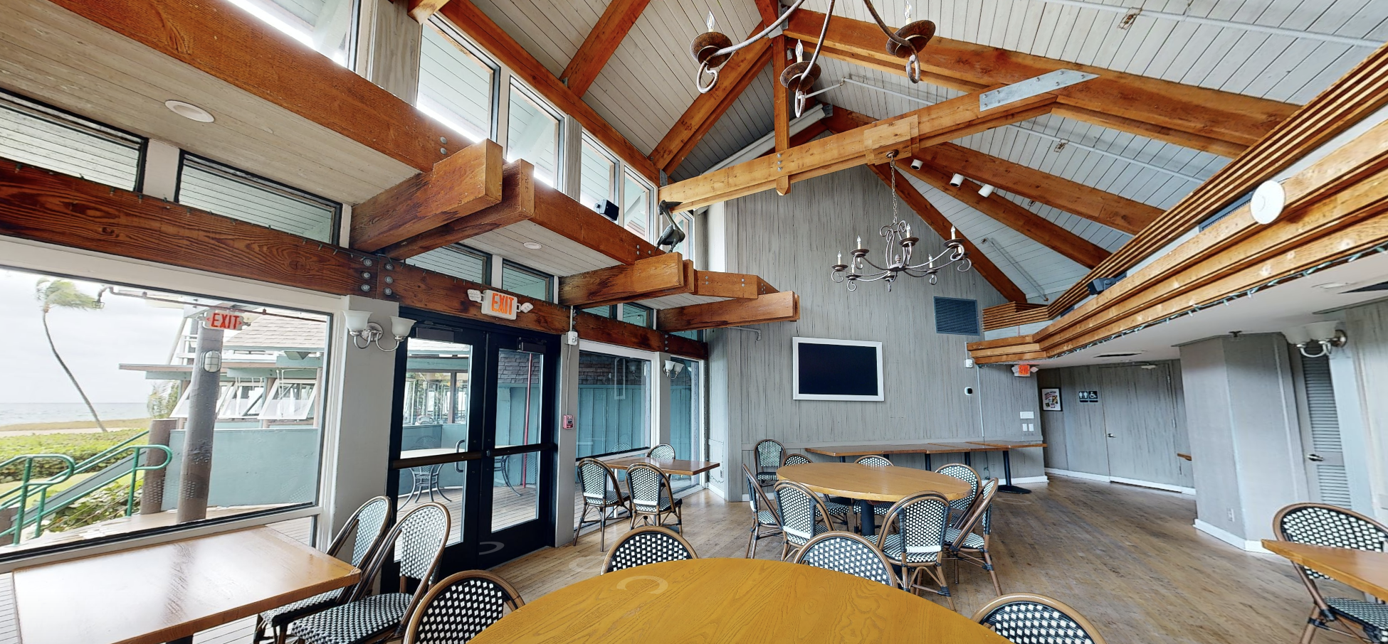 Laser-scan photo of a Sea Watch dining room showing the existing vaulted ceiling, exposed timber beams, wrought-iron chandeliers, ocean-view windows, and bistro seating.